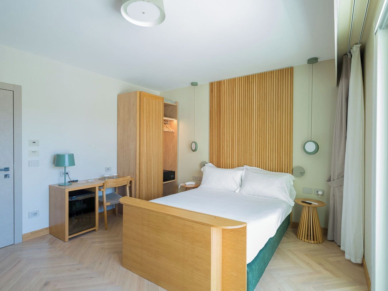 A hotel room with a bed, a desk, a chair, a wardrobe, and a small round table.