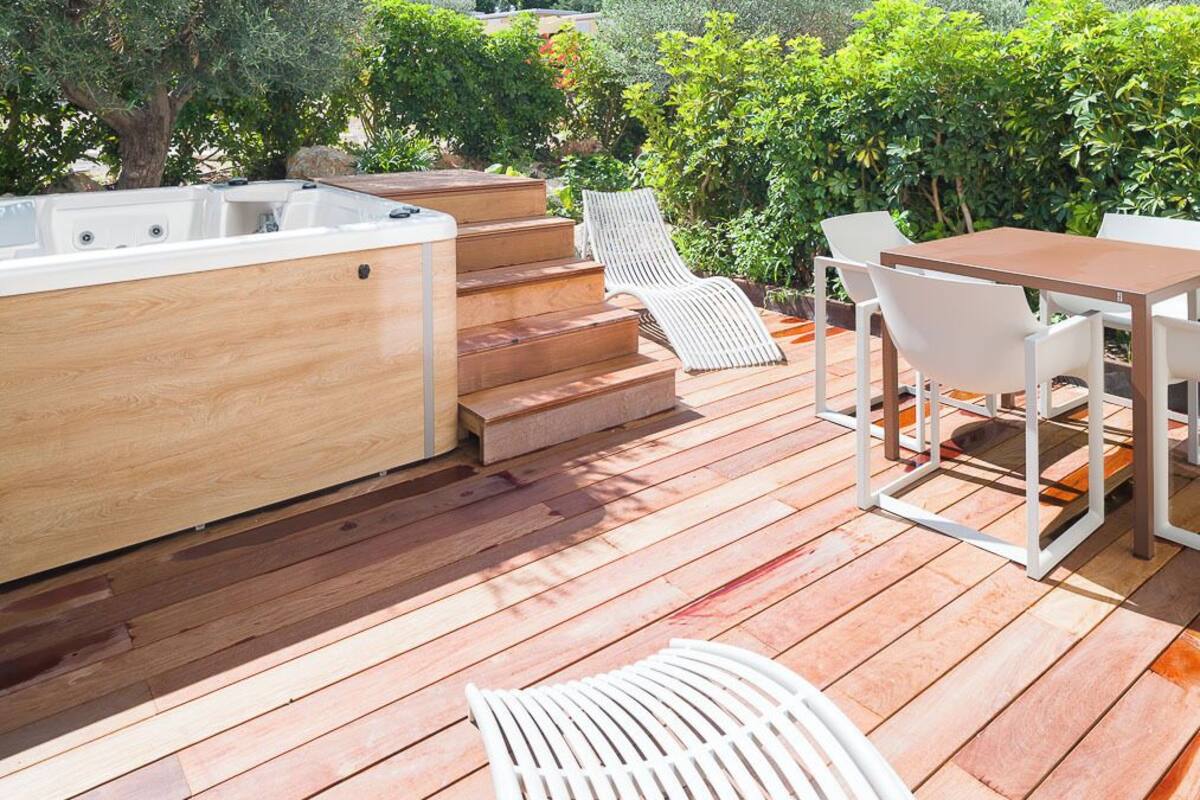 Um deck de madeira com hidromassagem, área de estar externa e vista para um penhasco rochoso.