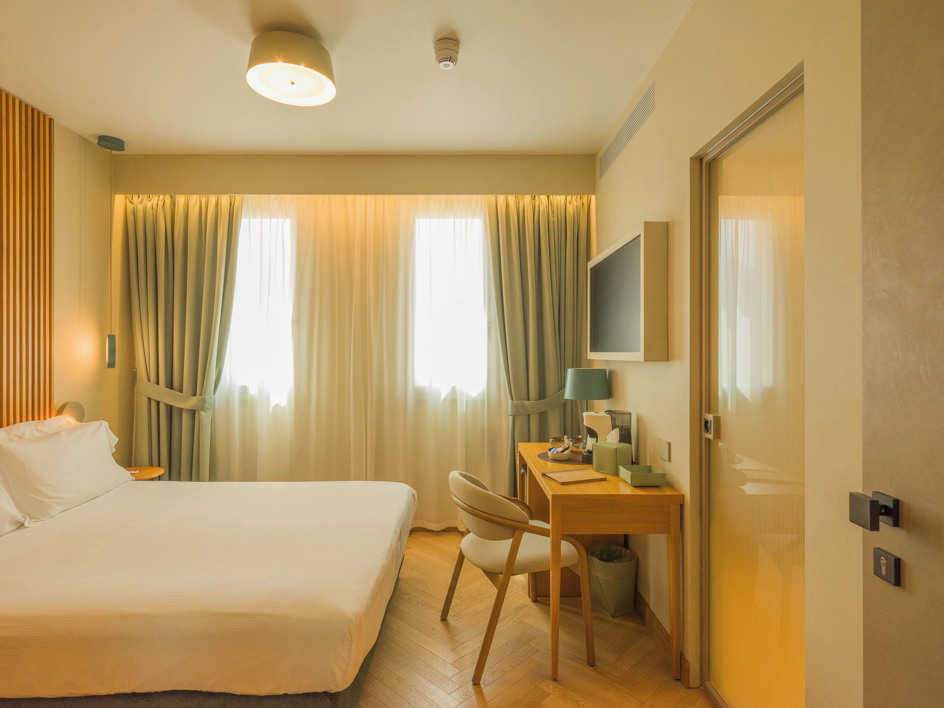 A hotel room with a bed, a desk, a chair, a television, and a door.