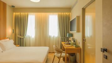 A hotel room with a bed, a desk, a chair, a television, and a door.