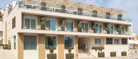 A modern hotel with a flat roof, multiple balconies, and outdoor seating areas.