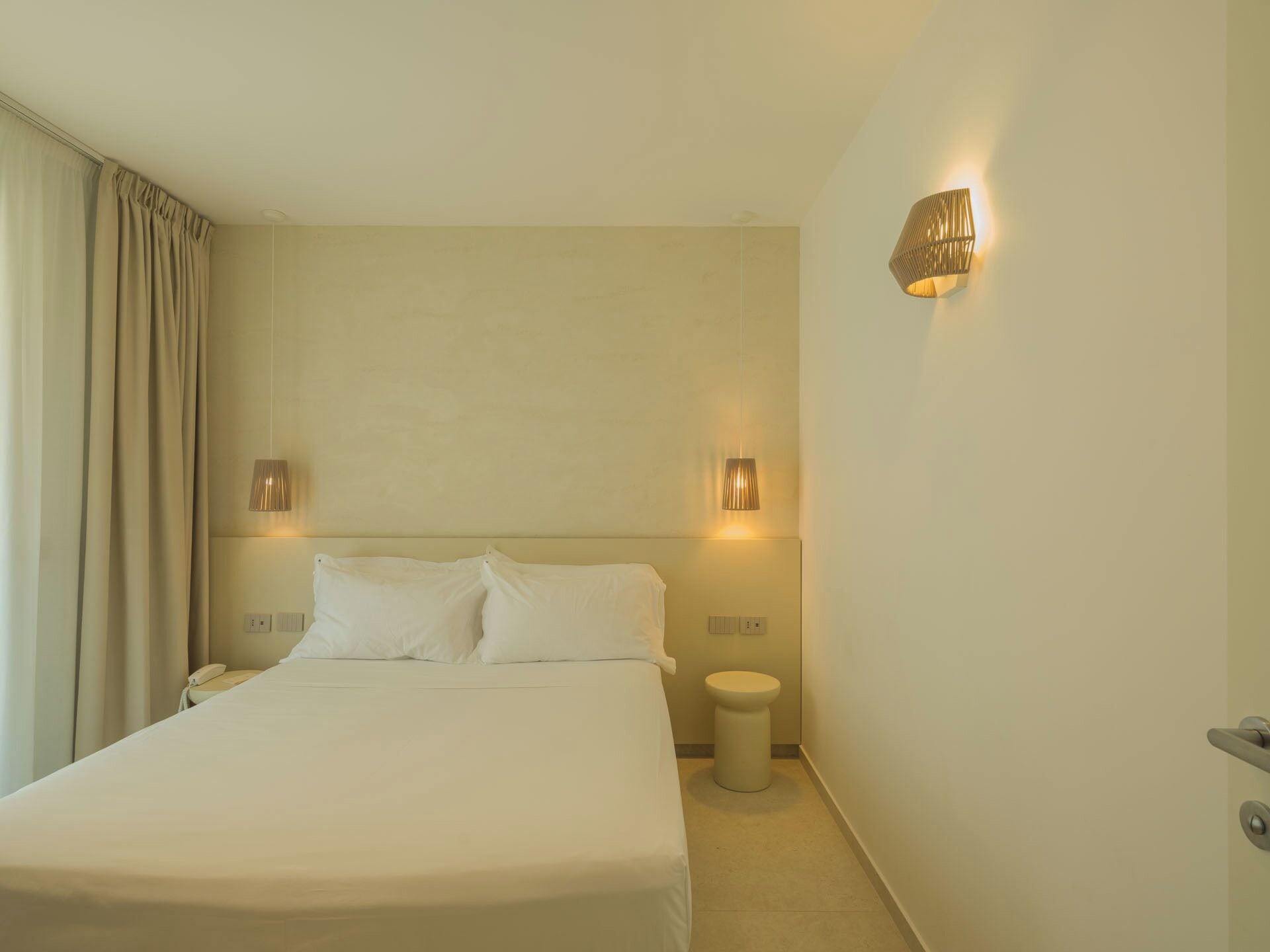 Una habitación de hotel con una cama grande, dos lámparas de noche, un teléfono en la mesita de noche y una pequeña mesita de noche.
