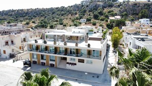 Un hotel moderno de varios pisos con terraza en la azotea, ventanas amplias y vistas a un paisaje montañoso.