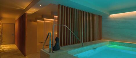 Un moderno espacio de spa con un jacuzzi, listones de madera y una persona sentada junto a la bañera.