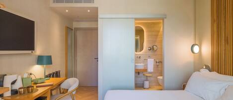 A hotel room with a bed, a desk, a chair, a mirror, a toilet, and a shower area.