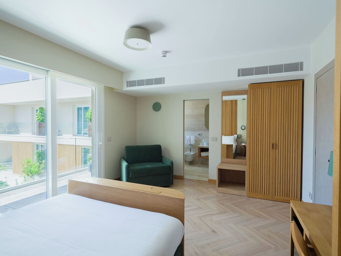 A hotel room with a bed, a chair, a bathroom, and a large window.
