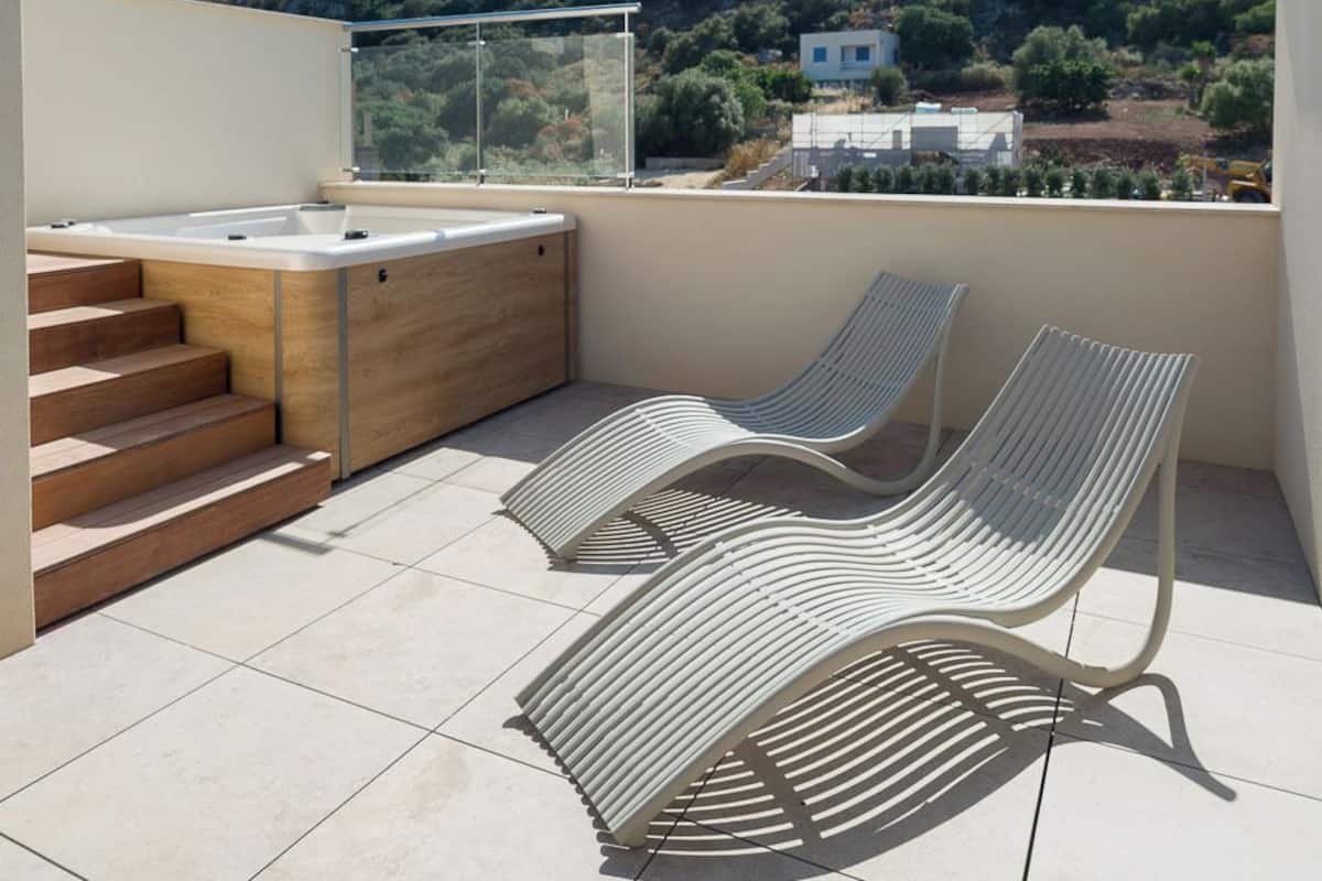 Terraço no telhado com banheira de hidromassagem, duas cadeiras de descanso e vista para uma colina.
