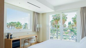 Habitación de hotel moderna con una cama grande, un escritorio con silla y vistas a palmeras y un parque.
