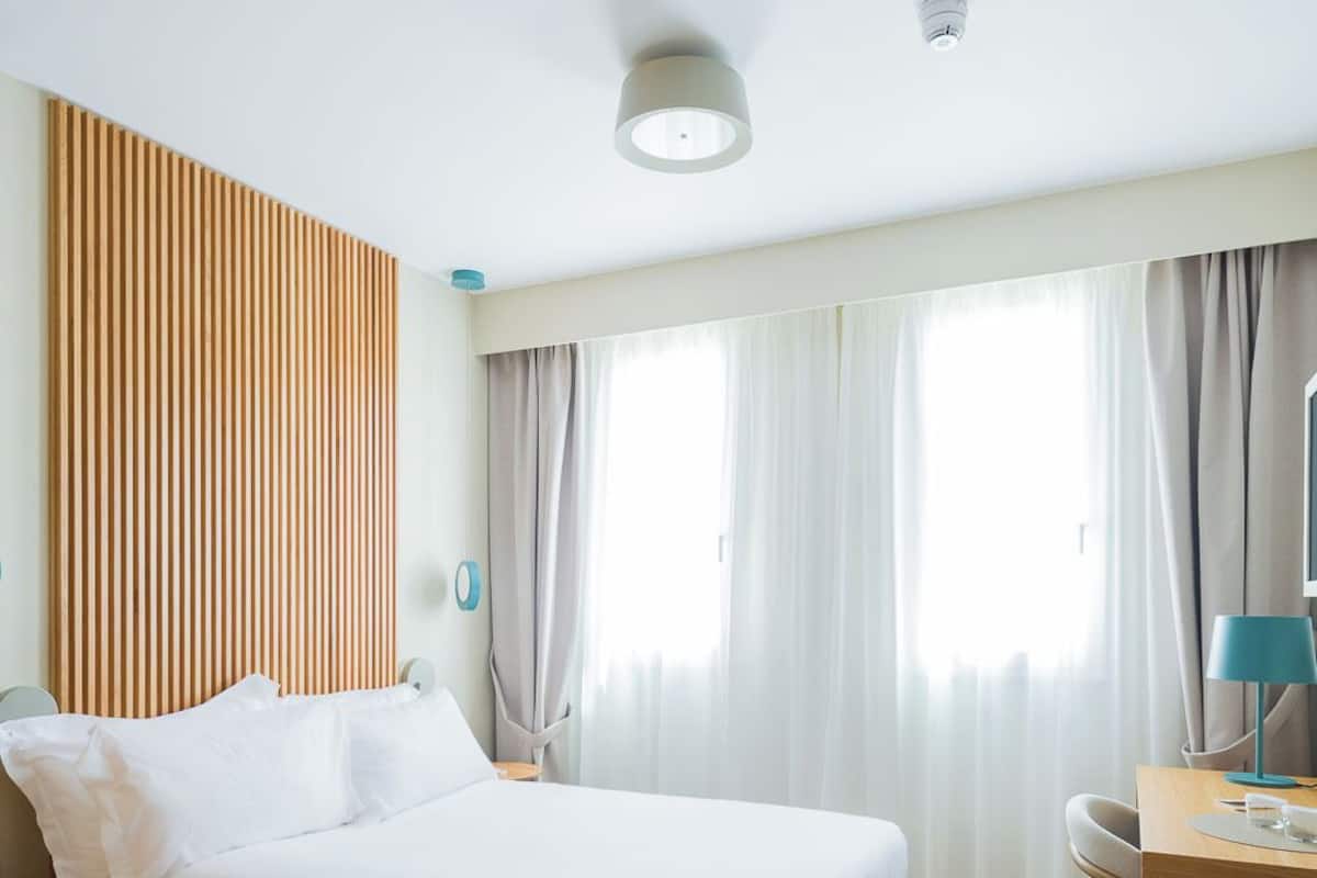 Quarto de hotel moderno com uma cama grande, uma escrivaninha e uma janela com cortinas.