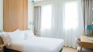 A modern hotel room with a large bed, a desk, and a window with curtains.