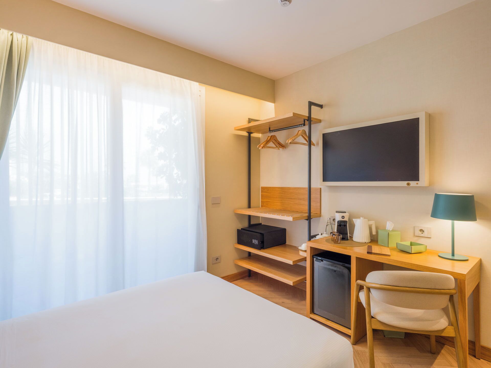 Ein Hotelzimmer mit einem Bett, einem Schreibtisch mit Lampe, einem Fernseher und einem Kleiderschrank mit Kleidung.