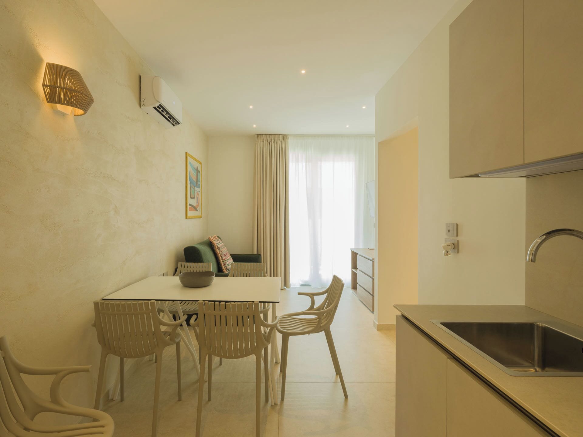 A modern kitchen with a stainless steel sink, a dining area with a table and chairs, and a large window with curtains.