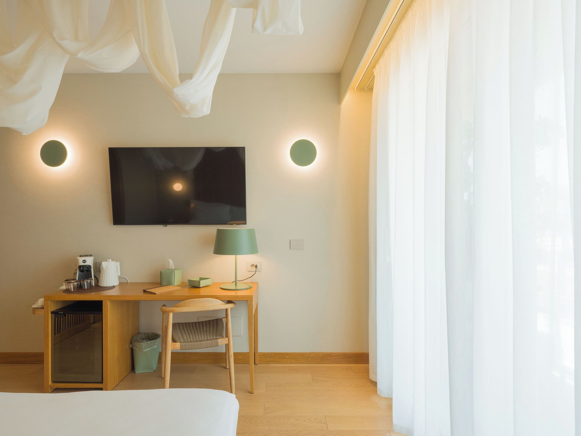 A hotel room with a bed, a desk with a lamp, a TV, and a window with curtains.