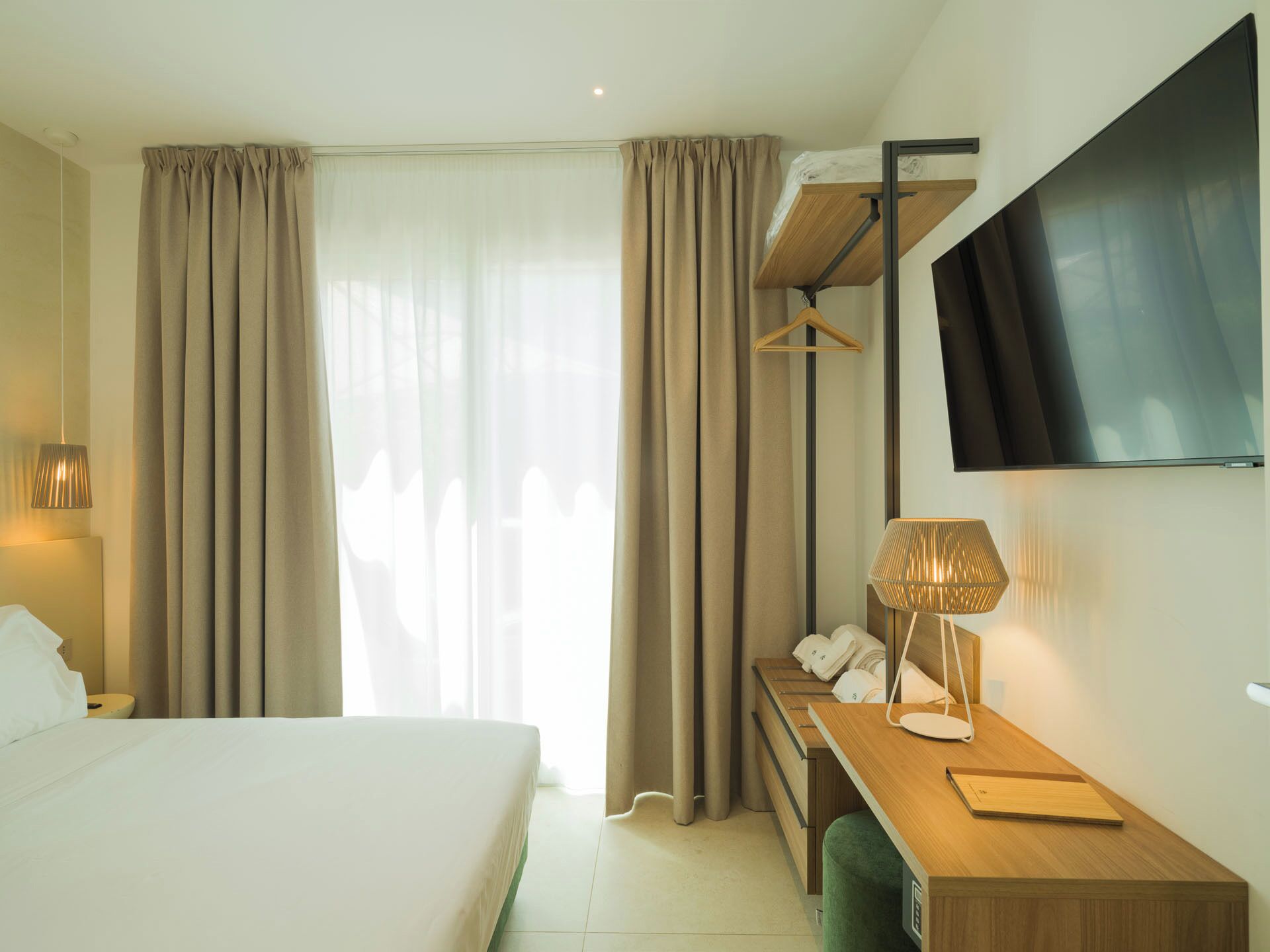 A hotel room with a bed, a desk, a TV, and a hanging coat rack.