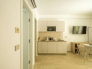 A modern kitchen with a microwave, coffee maker, and sink. There is a dining area with a table and chairs. - San Vito Resort & Spa (San Vito Lo Capo)