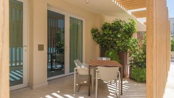 Un espacio exterior moderno con zona de estar, una mesa, sillas, una planta en maceta y un portón corredizo de vidrio que da a un balcón.