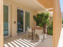 Un espacio exterior moderno con zona de estar, una mesa, sillas, una planta en maceta y un portón corredizo de vidrio que da a un balcón.
