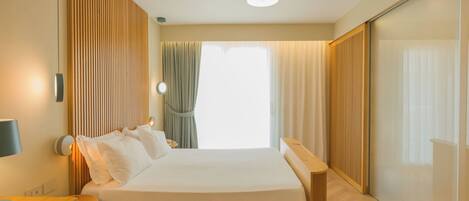 A modern hotel room with a bed, bedside table, lamp, and a view of the outside.