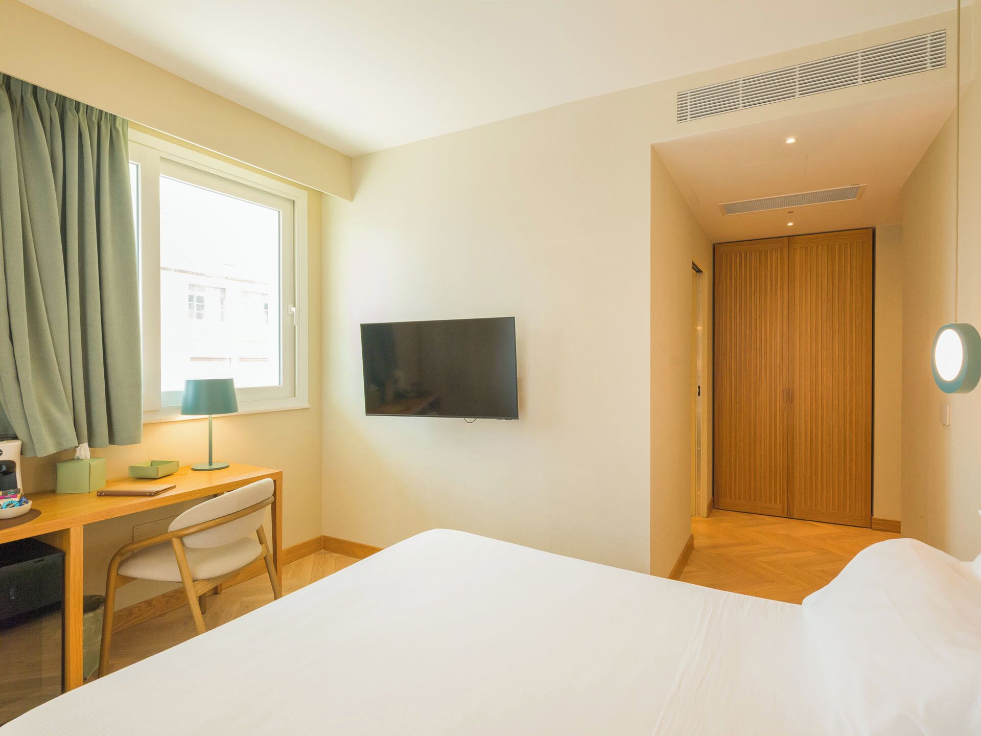 A hotel room with a bed, a desk with a chair, a television, and a wooden door.
