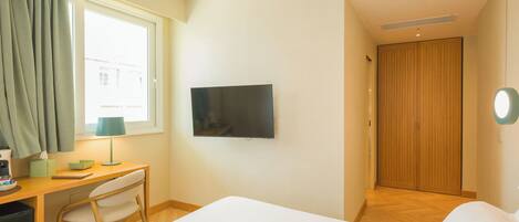 Una habitación de hotel con cama, escritorio con silla, televisión y puerta de madera.