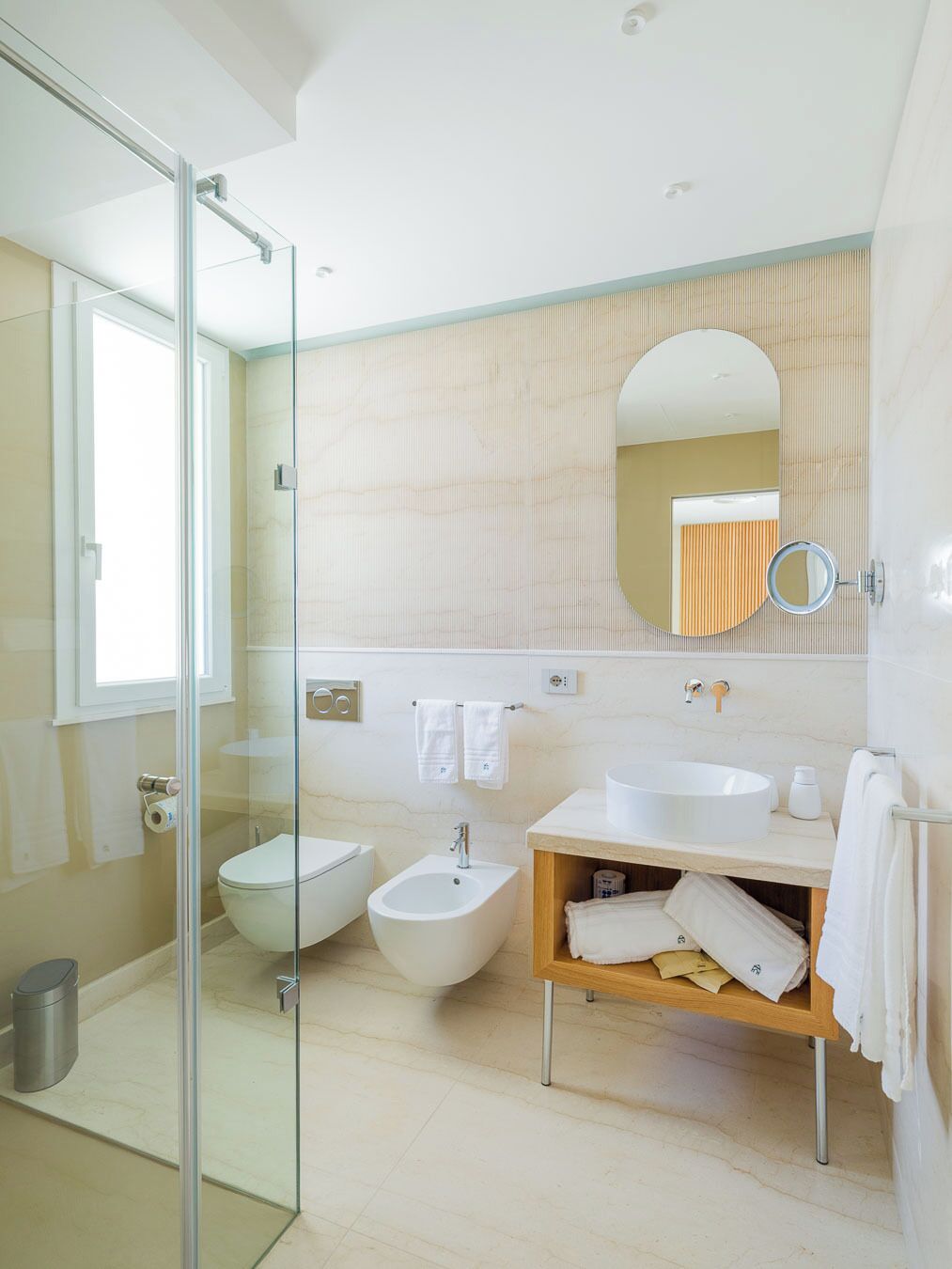A modern bathroom with a glass shower enclosure, a bidet, a sink, and a mirror.