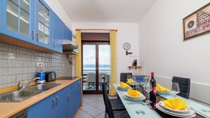 A modern kitchen with blue cabinets, a dishwasher, and a dining area set for two with yellow napkins and a wine bottle. - Apartman Sea Blue  (Crikvenica)