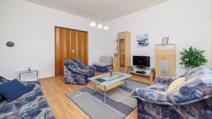 A modern living room with a sofa, armchair, coffee table, TV, and a plant. - Apartman Sea Blue  (Crikvenica)