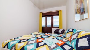A bedroom with a colorful quilted bedspread, a chair, and a window with curtains. - Apartman Sea Blue  (Crikvenica)