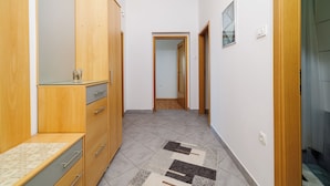 A hallway with wooden cabinets, a tiled floor, and a mirror. - Apartman Sea Blue  (Crikvenica)
