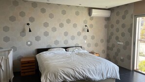 Une chambre moderne avec un grand lit, deux tables de chevet et un climatiseur fixé au mur.