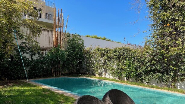 Une piscine entourée de chaises longues en osier et d’une pelouse.