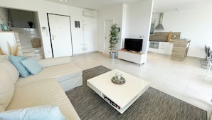 A modern living room with a sofa, coffee table, and TV. There is a kitchen area with cabinets and a dining table. - Apartment Bella (Crikvenica)
