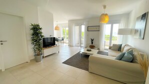A modern living room with a flat-screen TV, a sofa, a coffee table, and a dining area with chairs. - Apartment Bella (Crikvenica)