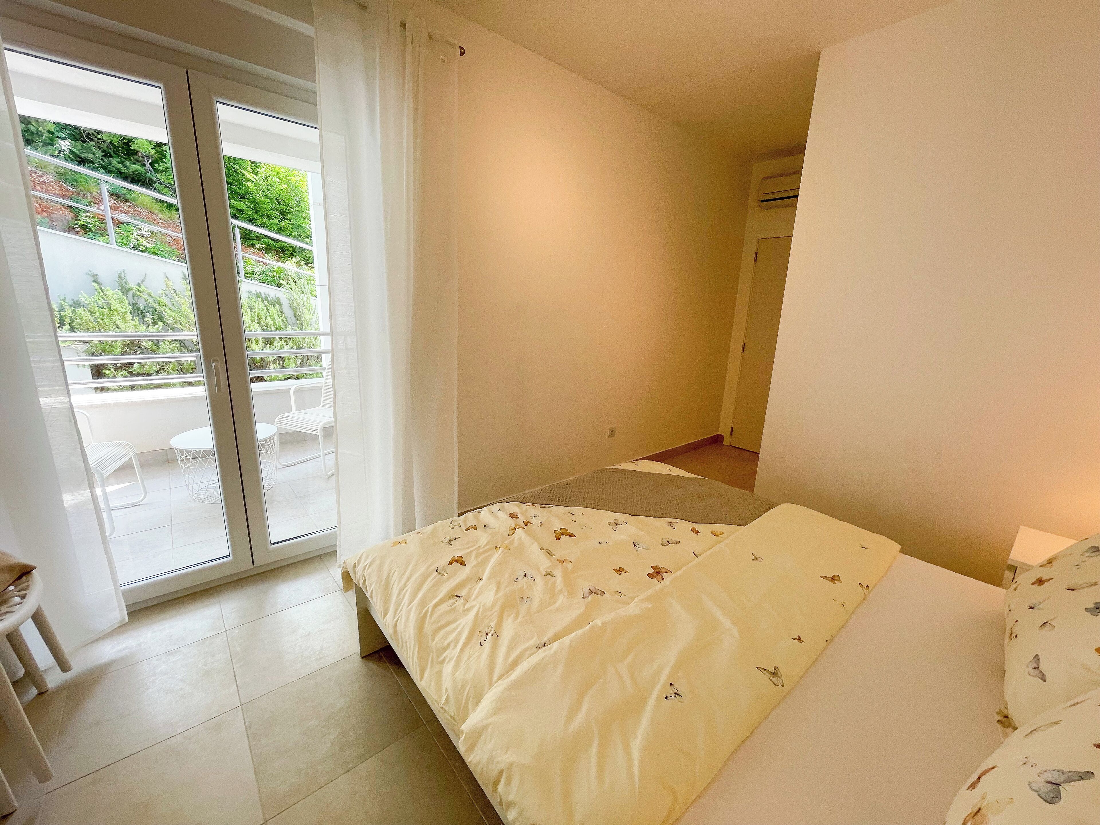A bedroom with a bed, a sliding glass door leading to an outdoor area with a chair and table, and a small window.