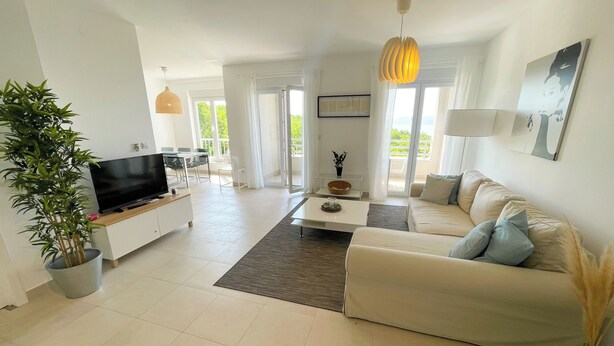 A modern living room with a flat-screen TV, a sofa, a coffee table, and a dining area with chairs and a table. - Apartment Bella (Crikvenica)