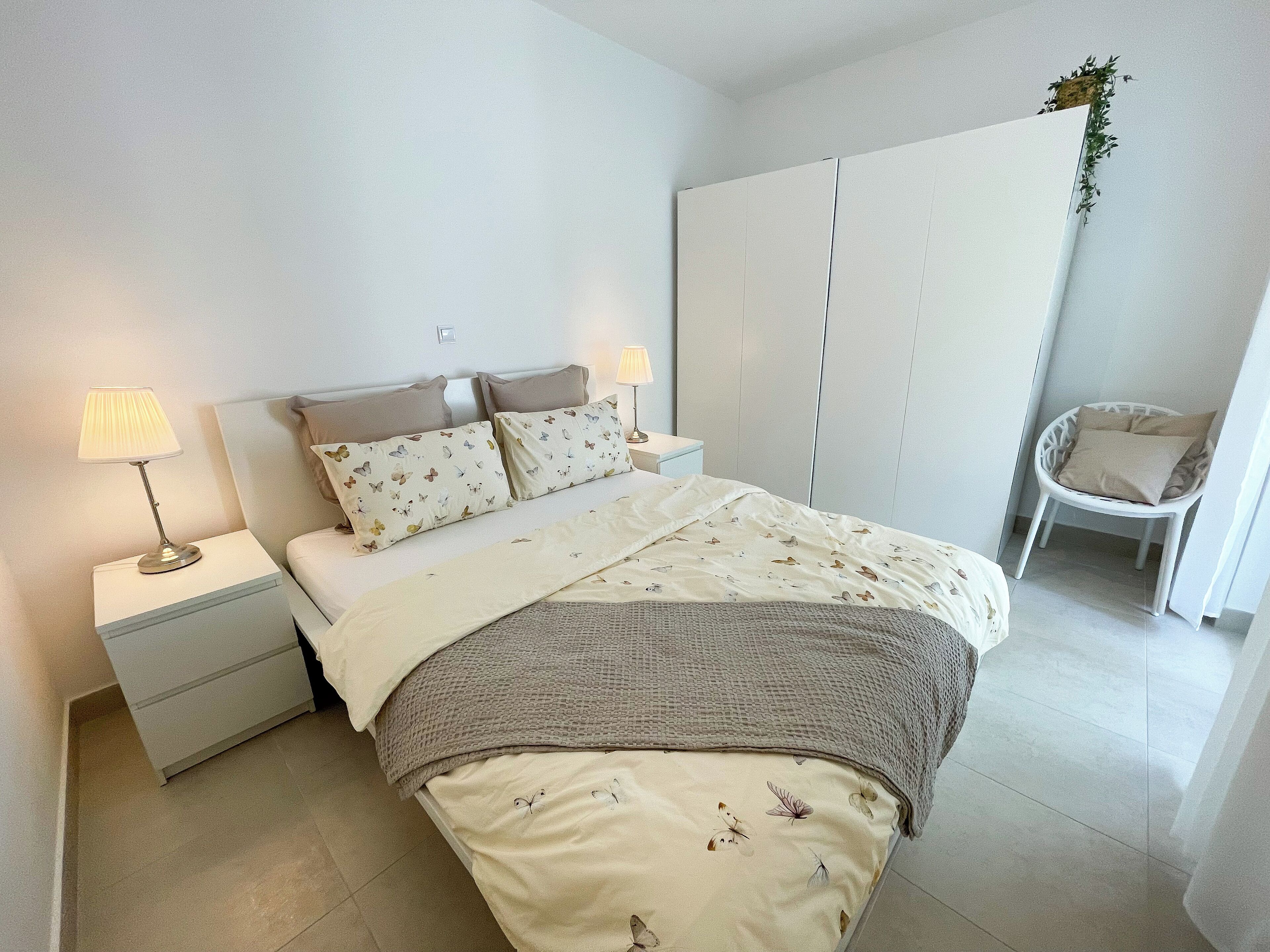 Una camera da letto ordinata con un letto, due comodini, una sedia e un armadio.