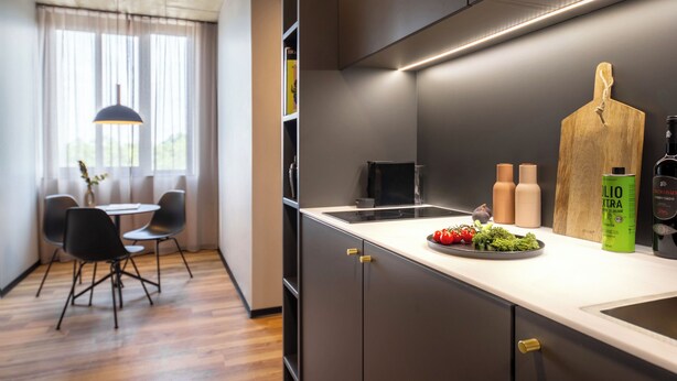 A modern kitchen with a built-in stove, a wooden cutting board, and a bottle of olive oil on the counter. - ipartment Koeln Oper @HOME by Best Western (Cologne)