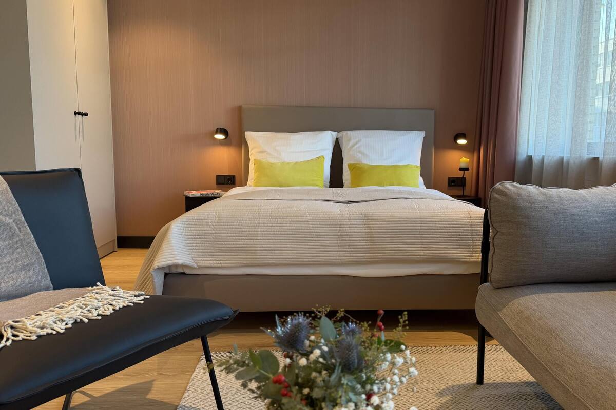 Une chambre d’hôtel comprenant un lit, deux tables de chevet, un canapé, un banc et une plante décorative.