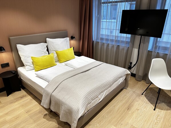 A hotel room with a bed, a TV, a chair, and a window with curtains. - ipartment Koeln Oper @HOME by Best Western (Cologne)