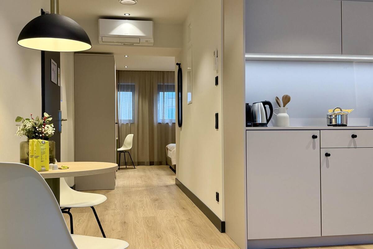 Une chambre d’hôtel moderne dotée d’un coin repas, d’une kitchenette et d’un couloir menant à une chambre à coucher.