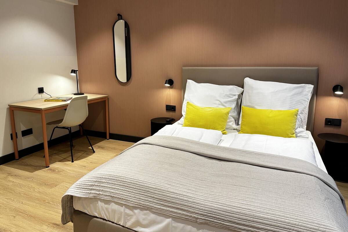 Une chambre d’hôtel équipée d’un lit, d’un bureau, d’une chaise, d’un miroir et de lampes de chevet.