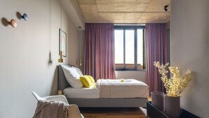 A modern bedroom with a bed, a bedside table, a chair, a window with curtains, and a view of the outside. - ipartment Koeln Oper @HOME by Best Western (Cologne)