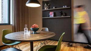 A modern dining area with a round wooden table, green chairs, a black pendant light, and a decorative bowl on the table. - ipartment Koeln Oper @HOME by Best Western (Cologne)