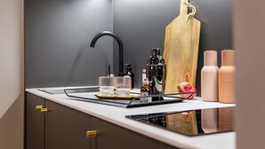 A modern kitchen with a sleek black faucet, a wooden cutting board, and a countertop with various items including a bottle, glasses, and a pomegranate. - ipartment Koeln Oper @HOME by Best Western (Cologne)