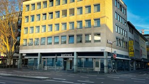 En bygning med flere etager, en flad facade, store vinduer og en indgang i stueplan med skiltet 'apartments'.