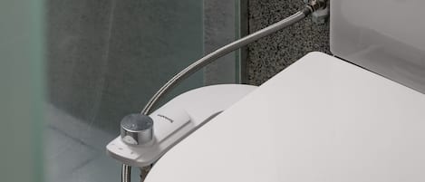 Un baño moderno con inodoro blanco, zona de ducha y puerta de cristal.