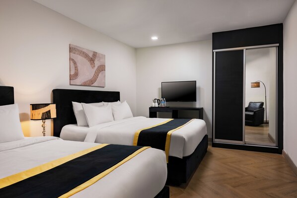 Habitació d'hotel amb dos llits, televisió de pantalla plana, cafetera i armari amb portes corredisses.