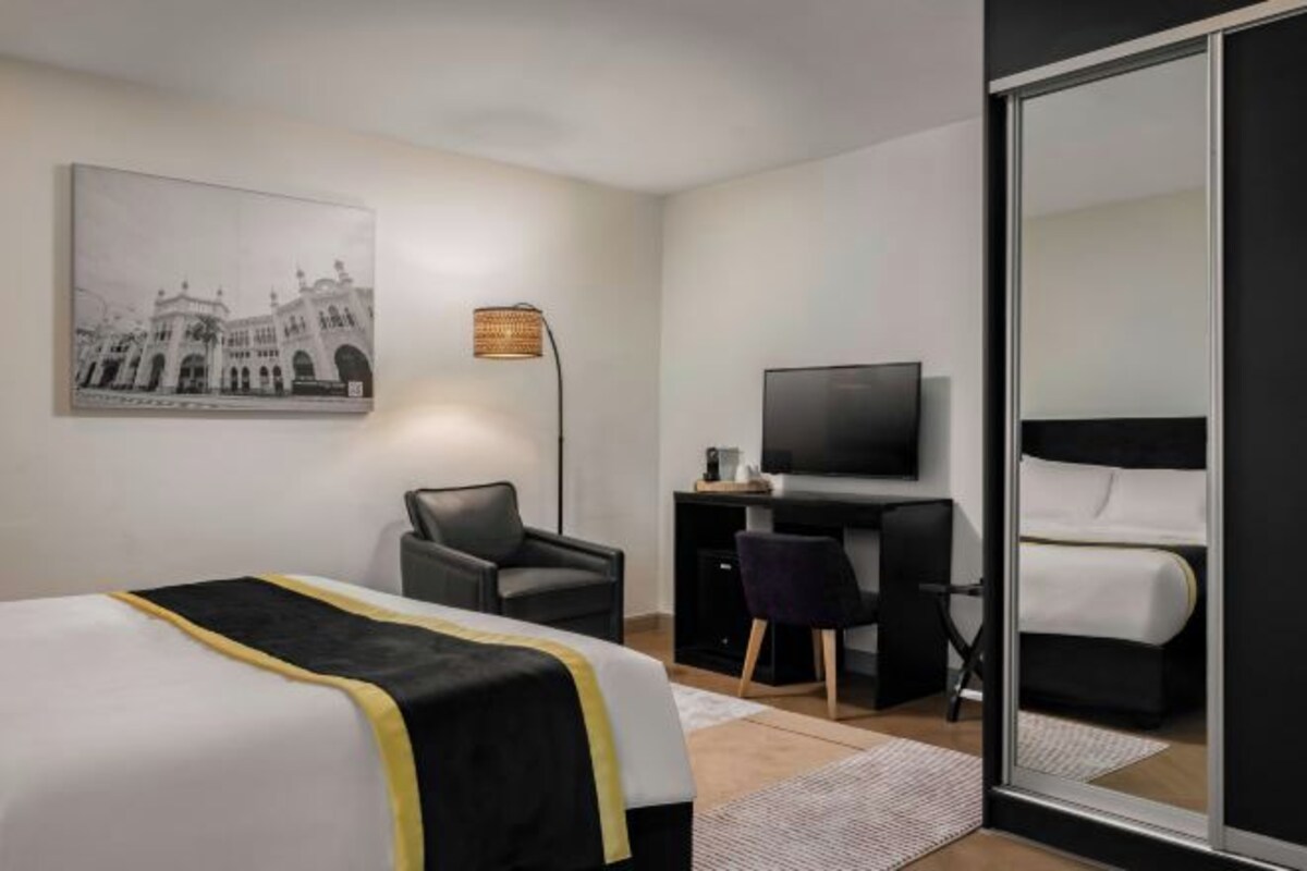 A modern hotel room with a bed, a desk, a chair, a television, and a large window.