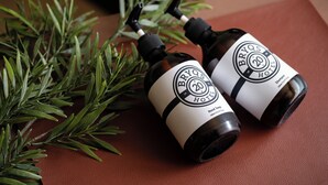 Two bottles of Bryos Hotel hand soap on a brown leather surface with green foliage. - BRYQs Hotel Kuala Lumpur (Kuala Lumpur)