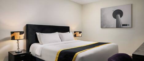 Habitación de hotel con cama, dos mesitas de noche, un sillón y una obra de arte en la pared.